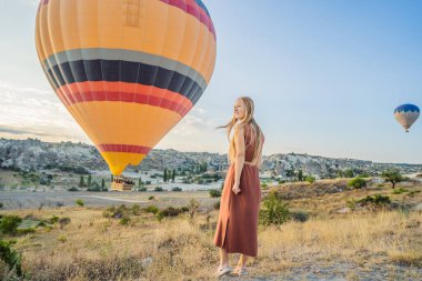 Kapadokya, Türkiye 'de sıcak hava balonlarına bakan turist kadın. İyi yolculuklar hindi konsepti. Dağın tepesinde harika manzaranın tadını çıkaran bir kadın.