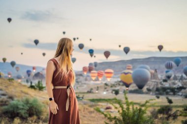 Kapadokya, Türkiye 'de sıcak hava balonlarına bakan turist kadın. İyi yolculuklar hindi konsepti. Dağın tepesinde harika manzaranın tadını çıkaran bir kadın.