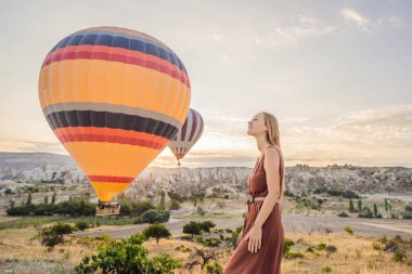 Kapadokya, Türkiye 'de sıcak hava balonlarına bakan turist kadın. İyi yolculuklar hindi konsepti. Dağın tepesinde harika manzaranın tadını çıkaran bir kadın.