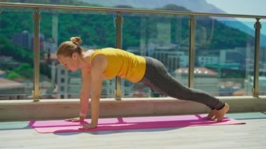 Young woman is practicing yoga on in modern apartment terace with mountains and sea in the background.