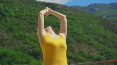 Young woman is practicing yoga on in modern apartment terace with mountains and sea in the background.