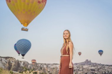 Kapadokya, Türkiye 'de sıcak hava balonlarına bakan turist kadın. İyi yolculuklar hindi konsepti. Dağın tepesinde harika manzaranın tadını çıkaran bir kadın.