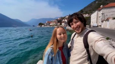 Karadağ 'ın Perast kentinde denizin kenarında duran mutlu genç adam ve kadın selfie videosu çekiyor. Çarpıcı bir katedral de dahil olmak üzere tarihi binalarla dolu olan kaldırım taşlı sokaklarını keşfediyorlar.