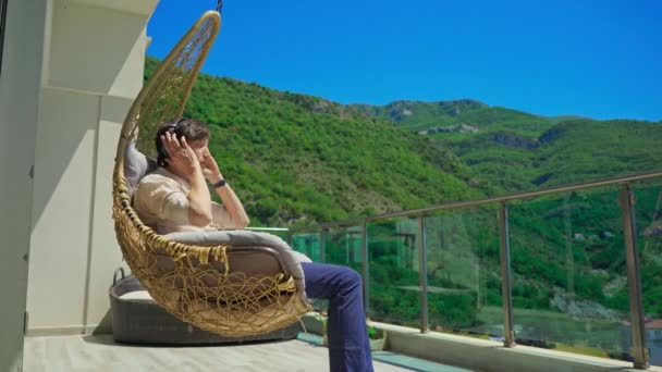 Young Man Balcony Enjoying Music Swinging Chair Mountain Scenery Background — Wideo stockowe