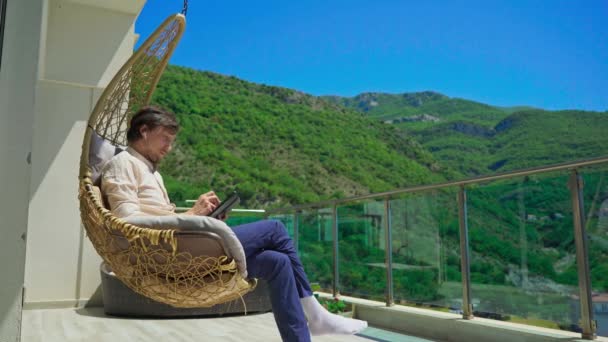 Joven Balcón Rodeado Paisajes Montaña Creando Tableta Una Cómoda Silla — Vídeos de Stock