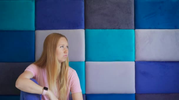 若い女性は カラフルなグレーとブルーの長方形の興味深い背景に囲まれています テキスト配置のためのフレーム内に十分なスペースがあります 彼女の表情は何かを思うと悲しみに変わる — ストック動画