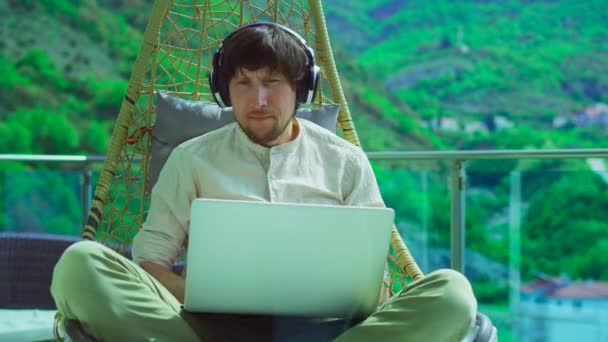Young Man Balcony Surrounded Mountain Scenery Wearing Headphones Focused Laptop — 图库视频影像