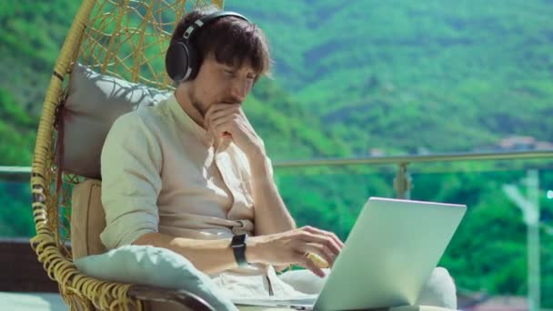 Young Man Balcony Surrounded Mountain Scenery Wearing Headphones Focused Laptop — 图库视频影像