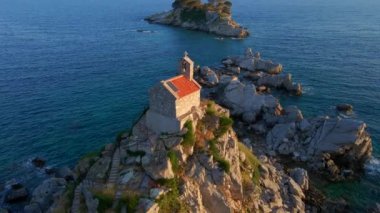 Yavaş çekim hava görüntüsü. Sveta Nedelja - Petrovac şehrine yakın küçük bir adadaki Hristiyan kilisesi Adanın üzerinde bir sürü kukla uçar.