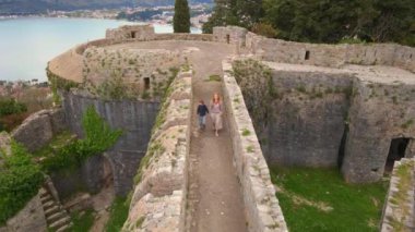 Yavaş çekim hava görüntüsü. Genç bir kadın ve oğlu turistler Herceg-Novi 'deki İspanyol kalesini veya Spanjola Kalesini ziyaret ediyorlar. Kalenin duvarlarında yürüyorlar. Karadağ 'a Seyahat.