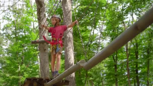 一个小男孩正在茂密的森林里 在一条绳索障碍物跑道上享受着令人兴奋的冒险 他带着头盔和安全带在充满挑战的航程中穿行 表现得很勇敢 — 图库视频影像