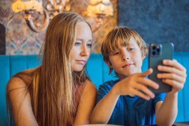 Umursayan genç anne, küçük oğlunla oturma odasında kanepede oturur, akıllı telefondan komik çizgi filmler izlersin, mutlu anne ya da dadı, küçük çocukla birlikte evdeki koltukta dinlenir, birlikte cep telefonu interneti kullanırız..