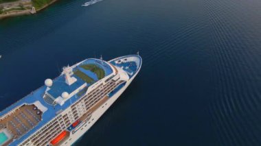 Yavaş çekim videosu. Güneş Boka-Kotor Körfezi 'nde batarken, limandan ayrılan beyaz bir yolcu gemisi arkasında hafif dalgalar bırakır. Dağların göz kamaştırıcı manzarası ve eski kasaba