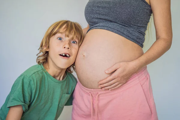 若い美しい妊婦と長男 そのかわいい少年は母親の腹に耳を傾けた 家族の概念で赤ちゃんを期待しています 若い子のために子供を準備する — ストック写真