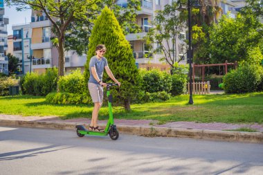 Şehirdeki arka planda elektrikli scooter kullanan genç bir adam. Kiralık elektrikli scooterlar..