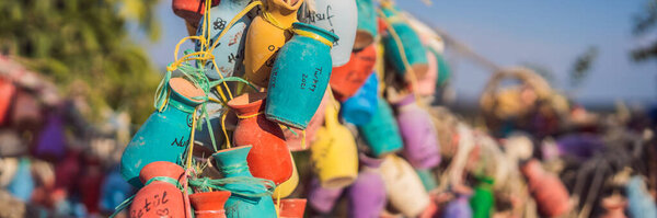 BANNER, LONG FORMAT Wish tree. Small multi-colored jugs with inscriptions, wishes hanging on the branches of a tree., against the backdrop of sand ruins and blue sky.
