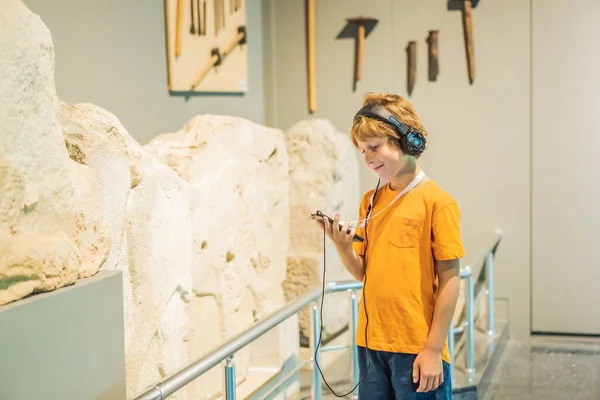Boy looking at sculptures and listening to audio guide at museum exhibition.
