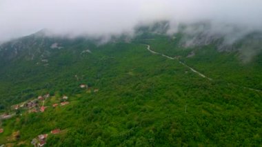 İnsansız hava aracı videosu alçak dağların ortasındaki, dolambaçlı bir yolu ve küçük bir Avrupa köyü olan geniş yeşil bir vadiyi nefes kesici bir şekilde yakalıyor. Gökyüzü bulutlarla kaplı ve İHA uçuyor