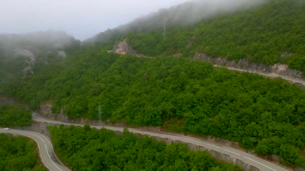 无人机相机带着观众穿过厚厚的云层 最终暴露了山口 云彩散去 一条弯弯曲曲的路出现了 通上山 四周一片茂密 — 图库视频影像