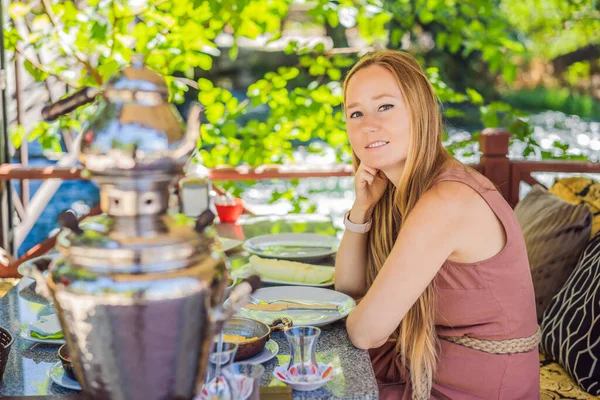 stock image woman tourist eat Turkish breakfast. Turkish breakfast table. Pastries. Vegetables. Olives. Cheeses, fried eggs. Jams, tea in copper pot and tulip glasses. Wide composition.