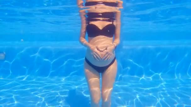 当一个孕妇站在游泳池里时 水下世界的宁静祥和的气氛环绕着她 女人的手在她的腹部形成了一个心形 显示了爱和联系 — 图库视频影像