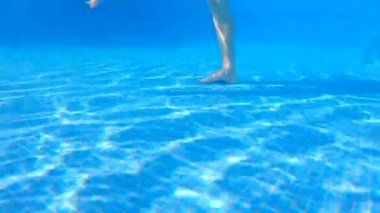 Bu yavaş çekim sualtı videosunda, hamile bir kadın yüzme havuzunda su egzersizleri yaparken görülüyor. Bebek çarpmasıyla, suyun içinde rahatça hareket ediyor, bunun faydalarını gösteriyor.