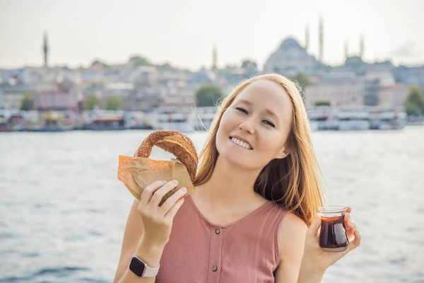 Woman in Istanbul having breakfast with Simit and a glass of Turkish tea. Glass of Turkish tea and bagel Simit against golden horn bay in Istanbul, Turkey. Turkiye.