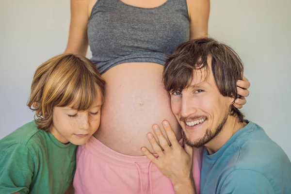 爸爸和大儿子听妈妈怀孕的肚子 — 图库照片