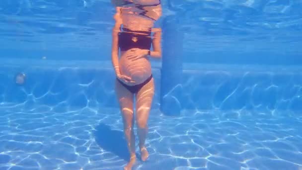 水中でのスローモーションビデオでは 妊娠中の女性が腕を腹の上に置き スイミングプールに立っています 水は彼女の周りを静かに流れる 水生演習の利点の概念 — ストック動画