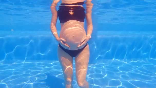 水中でのスローモーションビデオでは 妊娠中の女性が腕を腹の上に置き スイミングプールに立っています 水は彼女の周りを静かに流れる 水生演習の利点の概念 — ストック動画