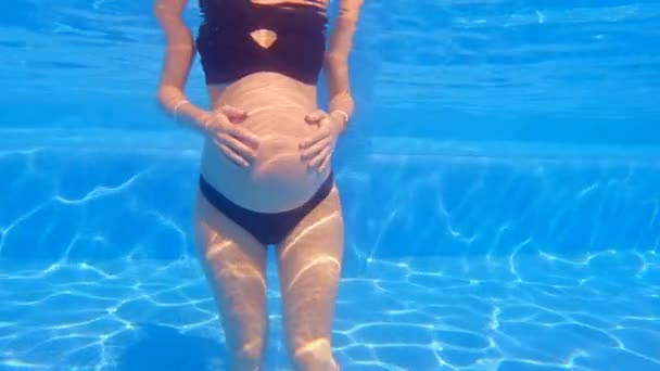 在这个慢动作的水下视频中 一个孕妇站在游泳池里 胳膊靠在肚子上 水在她周围缓缓流动 水上运动惠益的概念 — 图库视频影像