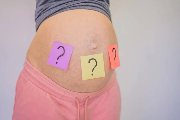 赤ん坊の名前を選ぶおなかの紙のステッカーに疑問符を持つ妊娠中の女性を混乱 — ストック写真