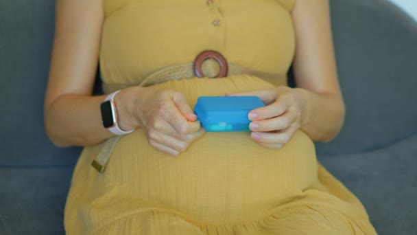 在这个慢镜头中 一个孕妇坐在沙发上 她从装有切片的塑料盒里吃一片维生素或食品补充剂 相机集中在她的手和 — 图库视频影像