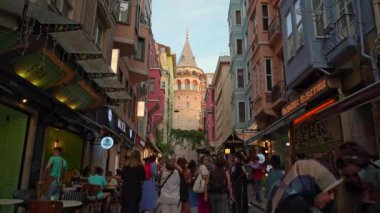 İstanbul 'da Galata Kulesi yakınlarındaki işlek cadde. Hızlandırılmış video, tarihi bölgeyi keşfeden turist kalabalığının coşkulu sahnesini kaydediyor. Renkli dükkanlar, kafeler ve sokak satıcıları