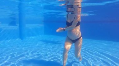 Bu yavaş çekim sualtı videosunda, hamile bir kadın yüzme havuzunda su egzersizleri yaparken görülüyor. Bebek çarpmasıyla, suyun içinde rahatça hareket ediyor, bunun faydalarını gösteriyor.