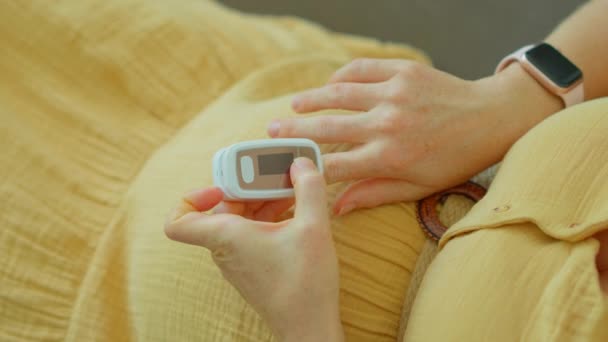 このビデオでは 妊娠中の女性がパルス酸素濃度計を使用して酸素濃度を測定しています スローモーション映像は彼女の指に置かれているデバイスをキャプチャし 読書を表示します — ストック動画