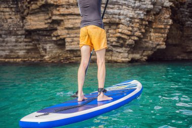 Genç erkekler, Karadağ 'daki kayaların arasında mavi sularda ayakta kürek çekerek eğleniyorlar. Çeviri:.
