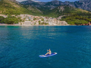 Genç kadınlar, Karadağ 'ın St. Stefan adası yakınlarındaki mavi denizde ayakta kürek çekerken eğleniyorlar. Çeviri:.