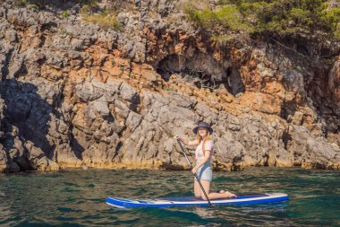 Genç kadınlar, Karadağ 'daki kayalıkların arasında mavi sularda ayakta kürek çekerken eğleniyorlar. Çeviri:.