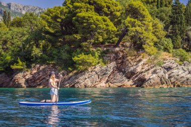 Genç kadınlar, Karadağ 'ın St. Stefan adası yakınlarındaki mavi denizde ayakta kürek çekerken eğleniyorlar. Çeviri:.