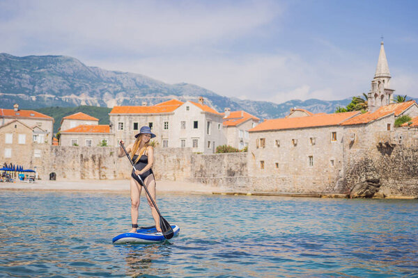 Young women Having Fun Stand Up Paddling in blue water sea in Montenegro. Against the backdrop of the Old Town of Budva. SUP.