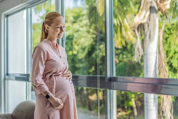 窓の近くに立っている若い妊婦の肖像画は コピースペースを持つ現代の家で彼女の腹に手を握っている 期待と優しさの概念 — ストック写真
