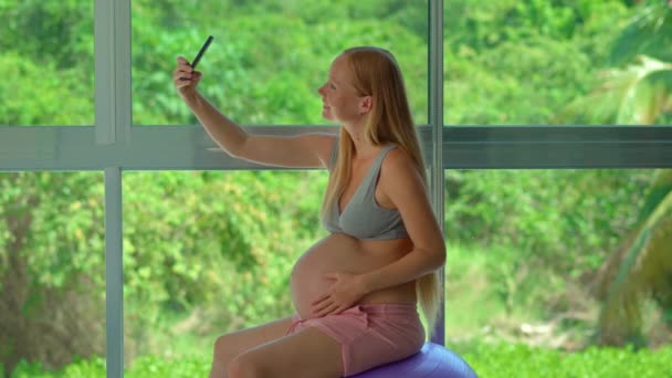 Una Mujer Embarazada Con Teléfono Inteligente Sienta Una Bola Forma — Vídeos de Stock