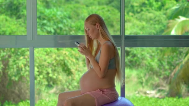 Egy Terhes Kecsesen Egy Fitt Labdán Egy Nagy Ablak Előtt — Stock videók