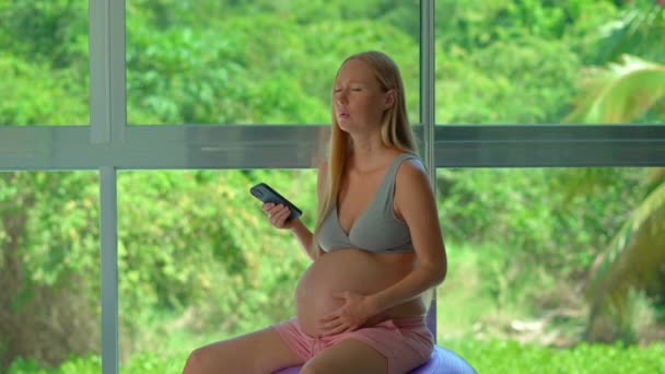 Gravid Kvinna Svänger Glatt Passform Boll Framför Ett Stort Fönster — Stockvideo