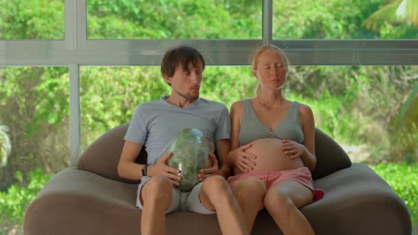 このユーモラスなスローモーションビデオでは 妊娠中の女性が自宅の腹にスイカを吹き付け 妊娠の体重と経験を軽くシミュレーションしました 彼らは一緒に座っている — ストック動画
