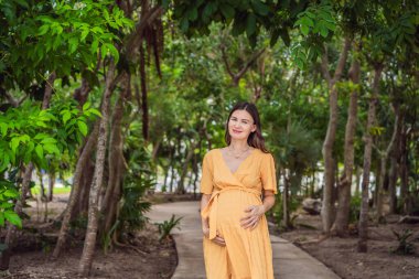 40 'ından sonra dingin ve ışıl ışıl hamile bir kadın, parkta güzelliklerle çevrili, parıldayan bir gülümsemeyle annelik yolculuğuna değer veren..