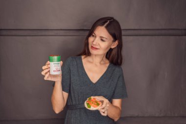 Almanya Berlin, 01.06.23: Kadın süper omega beslenme takviyeleri taşıyor. 40 yaşını geçmiş düşünceli hamile bir kadın balık mı yemeli yoksa omega 3 kapsülünü mü seçmeli sağlıklı ve besleyici olmalı diye düşünüyor.