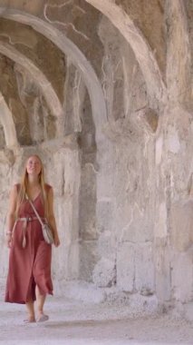 Dikey video. Hikaye biçimi. Genç bir kadın turist antik Roma tiyatrosu Aspendos 'un sütunlu galerisinin içinde yürüyor. Türkiye kavramına yolculuk.