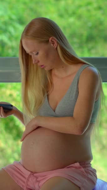 バーティカルビデオ ストーリーフォーマット この美しいスローモーションストックビデオでは 妊婦が活気に満ちた熱帯の風景を見下ろす大きな窓の前にフィットボールの上に座っています シーンキャプチャー — ストック動画